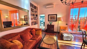 Una sala de estar con un sofá rojo, una mesa de centro, una estantería y un amplio ventanal con cortinas.