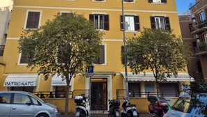 A yellow building with multiple windows and a door, parked cars, and two trees in front. - Large romantic apartment near Trastevere with terrace 5 min from villa Panfili (Roma)
