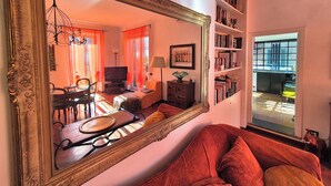 Una sala de estar con un espejo grande, un sofá, una mesa de comedor con sillas, un televisor y una estantería.