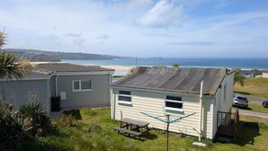 A coastal view with a beach, a small house with a sloped roof, and a picnic table. - D47 Chy-an-tewennow, Riviere Towans (Hayle)