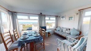 A cozy room with a dining table set for four, a sofa, and a TV. - D47 Chy-an-tewennow, Riviere Towans (Hayle)