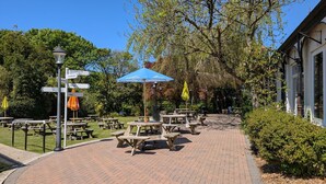 A paved pathway with picnic tables and umbrellas, surrounded by greenery and trees. - 37 Trevithick Court, Tolroy Manor (Hayle)