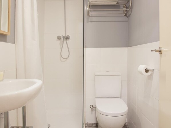 Un bany amb un lavabo blanc, un vàter i una dutxa amb porta de vidre.