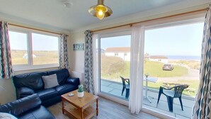 Ein Wohnzimmer mit einer schwarzen Ledersofa, einem Holztisch und Meerblick durch große Fenster.