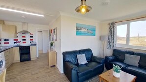 Ein kompakter Wohnbereich mit Küchenzeile, zwei Sofas, einem Couchtisch und einem großen Fenster mit Blick ins Freie.