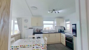 A compact kitchen with white cabinets, a washing machine, a microwave, a stove, and a sink. - B04 Beachcroft (B4), Riviere Towans (Hayle)