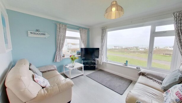 A living room with a sofa, a coffee table, a TV, and a 'WELCOME' sign. - B04 Beachcroft (B4), Riviere Towans (Hayle)