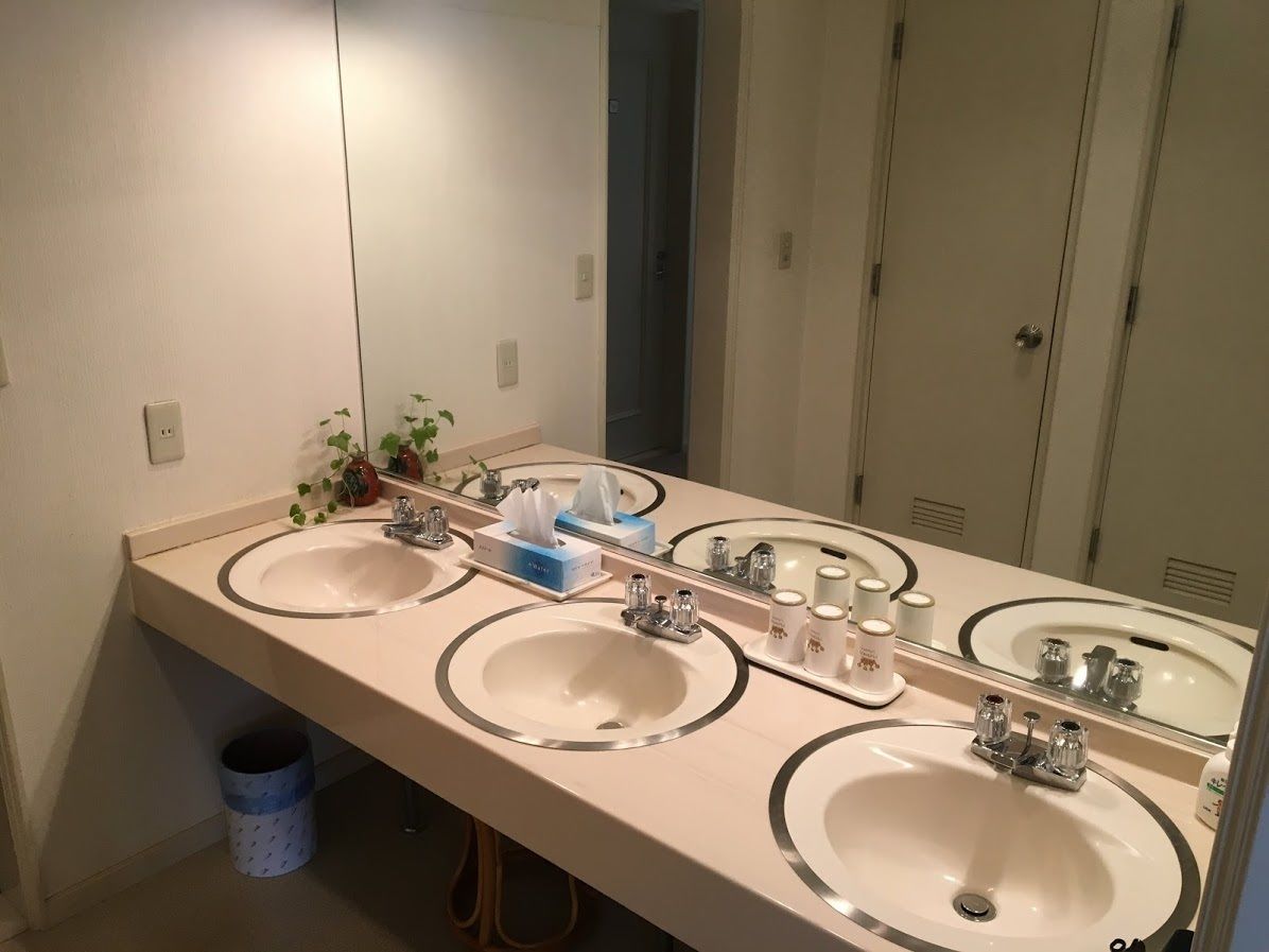Un baño con tres lavamanos, un espejo y un bote de basura.