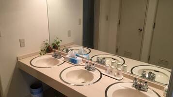 Un baño con tres lavamanos, un espejo y un bote de basura.