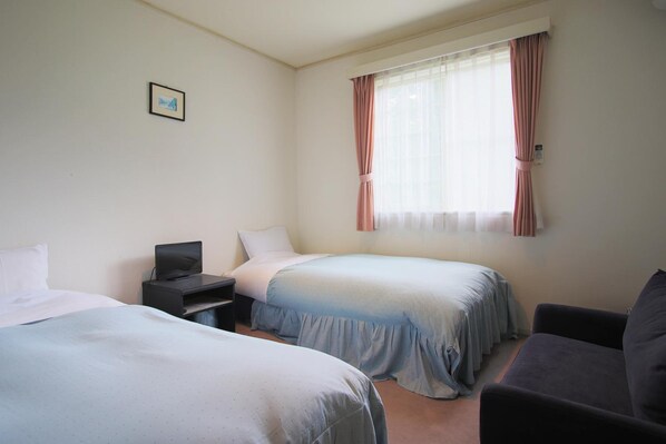 A hotel room with two beds, a desk with a laptop, a chair, and a window with curtains.