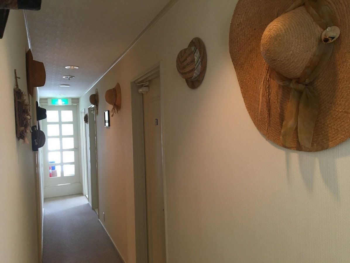 Un pasillo con una puerta al final, una lámpara en el techo y un sombrero colgado en la pared.