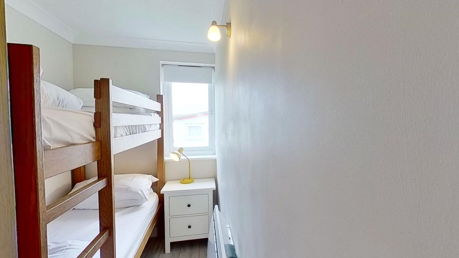 A bunk bed room with a bedside table and lamp, a window with a view, and a door.