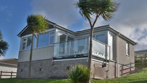 A two-story house with a balcony, stone foundation, and palm trees. - D29 Westbourne, Riviere Towans (Hayle)