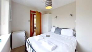 A bedroom with a bed, a bedside table, a wardrobe, and a door leading to another room. - D29 Westbourne, Riviere Towans (Hayle)