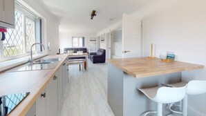 A modern kitchen with a wooden countertop, white cabinets, and a dining area with a sofa and chairs. - B51 Blue Bay, Riviere Towans (Hayle)