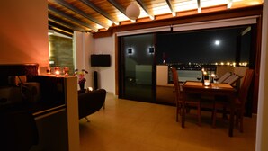 Un coin repas avec une table et des chaises, un téléviseur fixé au mur et une vue sur la ville la nuit.