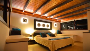 Une chambre moderne avec un grand lit, des poutres en bois au plafond et un luminaire fixé au mur.