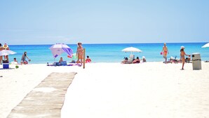 Une plage avec une promenade en bois menant à l’eau, des gens se détendant sous des parasols et des chaises de plage le long du rivage.