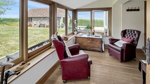 A spacious room with large windows, a wooden desk, two red armchairs, and a view of a stone building and garden. - Splatt Barn, Porlock (Porlock)