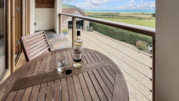 A wooden table with a bottle of wine and a glass on a balcony overlooking a scenic landscape. - Splatt Barn, Porlock (Porlock)