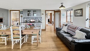 A modern kitchen with grey cabinets, a dining area with a wooden table and chairs, and a black leather sofa with a colorful blanket. - Splatt Barn, Porlock (Porlock)