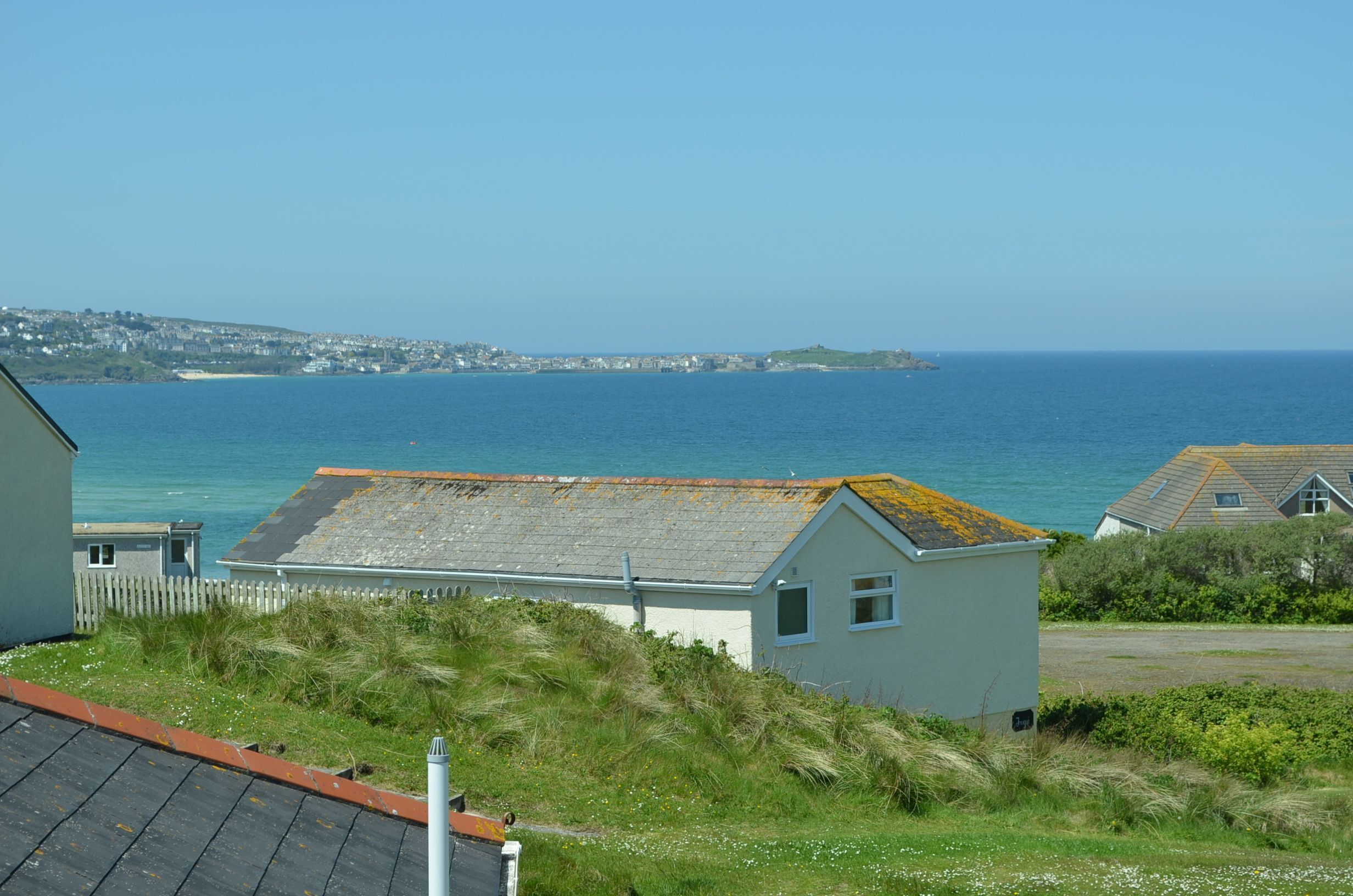 A coastal view with a house, grassy area, and a clear blue sea.