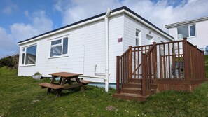 A mobile home with a wooden deck and picnic table, a small fenced area, and a clear sky. - E17 Glenvale, Riviere Towans (Hayle)