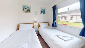 Une chambre avec deux lits, une table de chevet, une lampe et une fenêtre avec des rideaux.