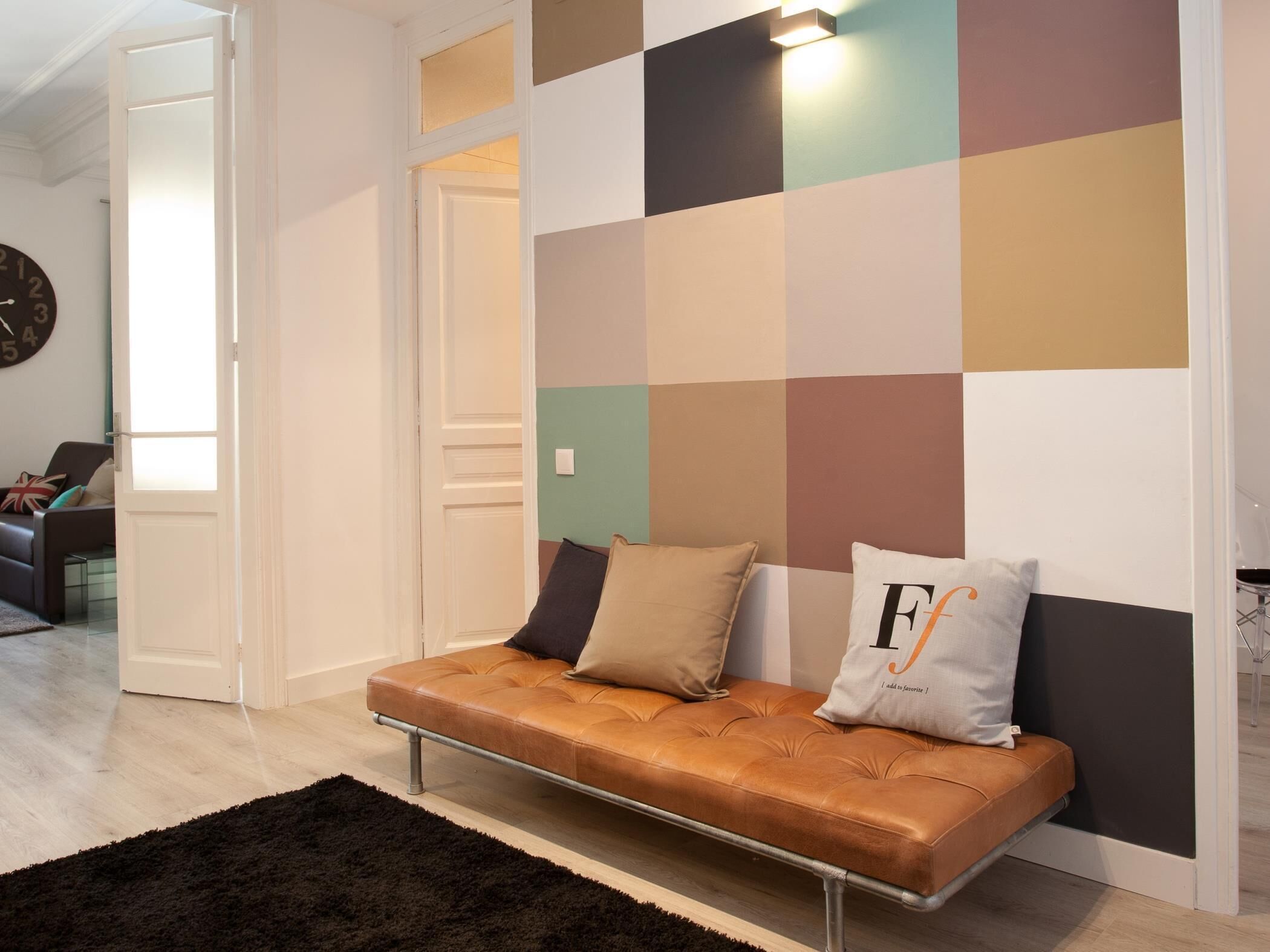 A modern living room with a sofa against a wall with a geometric pattern, a dark rug, and a clock on the wall.