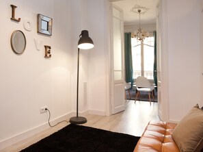 A modern living room with a black rug, a leather sofa, a standing floor lamp, and a chandelier.