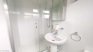 Et badeværelse med en glasvæg omkring bruseren, en hvid vask og et spejl over vasken.