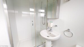 Bathroom features a glass-enclosed shower, pedestal sink, and wall-mounted faucet.