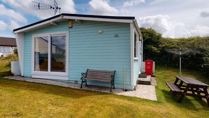 En lille, lyseblå hytte med en stor skydedør, en bænk udenfor og et picnicbord.