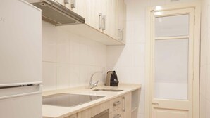 Une cuisine compacte équipée d’un réfrigérateur, d’un évier à deux bacs, d’un four et d’une porte dotée d’une grille d’aération.