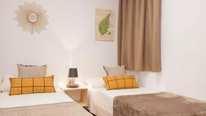Une chambre avec deux lits, une table de chevet avec une lampe, un miroir fixé au mur et une illustration botanique encadrée.