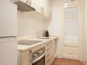 A compact kitchen with a refrigerator, stove, sink, and a coffee machine.