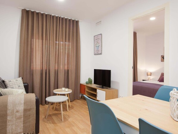 A furnished room with a sofa, a small round table, a TV, a desk, and a bed.
