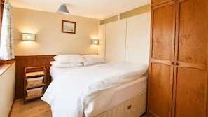 A bedroom with a bed, wooden wardrobe, wall-mounted lights, and a framed picture. - C19 Old Range, Riviere Towans (Hayle)