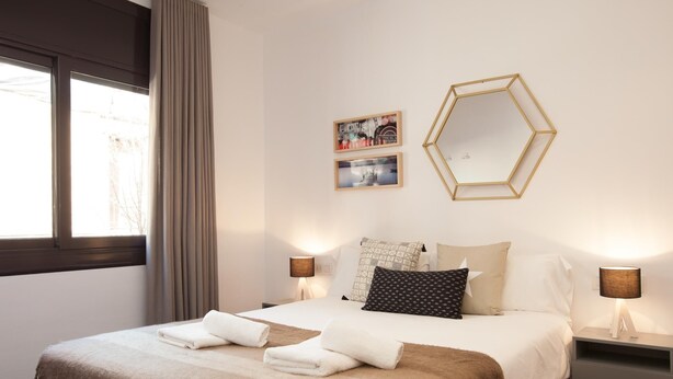 Habitación de hotel con una cama grande, dos lámparas de noche, un ventanal con cortinas y dos cuadros colgados en la pared.