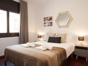 A hotel room with a large bed, two bedside lamps, a window with curtains, and two wall-mounted pictures. - Europa Fira Apartment 12 (L'Hospitalet de Llobregat)