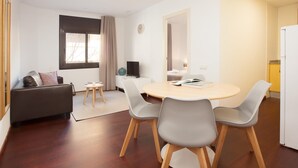 Una sala de estar moderna con un sofá, una mesa de comedor con sillas, un televisor y una zona de cocina con un refrigerador.