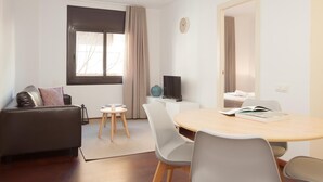 Una sala de estar moderna con un sofá, una mesa de comedor redonda con sillas, un televisor y una ventana con cortinas.