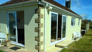 Ein kleines, eingeschossiges Haus mit Natursteinfassade, großen Schiebeglastüren und einer kleinen Veranda.