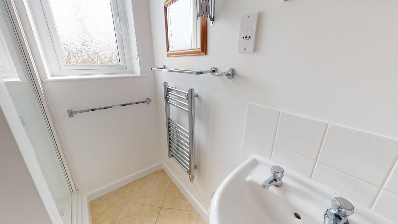 A bathroom with a bathtub, a towel rack, a radiator, a window, and a mirror.