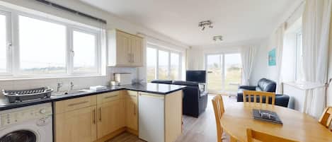 A modern kitchen with a dishwasher, washing machine, and a dining area with a table and chairs.