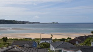 Blick auf die Küste mit einem Sandstrand, blauem Himmel und Wohnhäusern im Vordergrund.