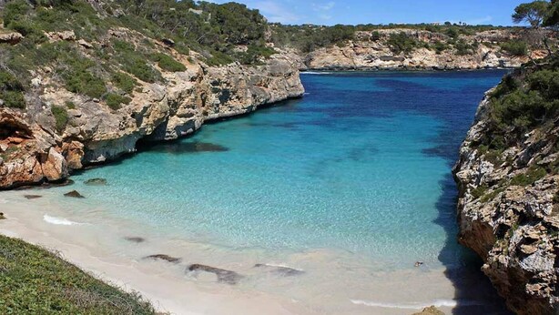 Eine Küstenlandschaft mit klarem türkisblauem Wasser, felsigen Klippen und einem Sandstrand.