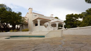 Eine weiße Villa mit Swimmingpool, umgeben von Palmen und einer Steinterrasse.