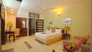 A hotel room with a bed, a desk, a chair, a sofa, a glass coffee table, a fruit basket, and a vase with flowers. - Well Park Residence Boutique Hotel (Chittagong)