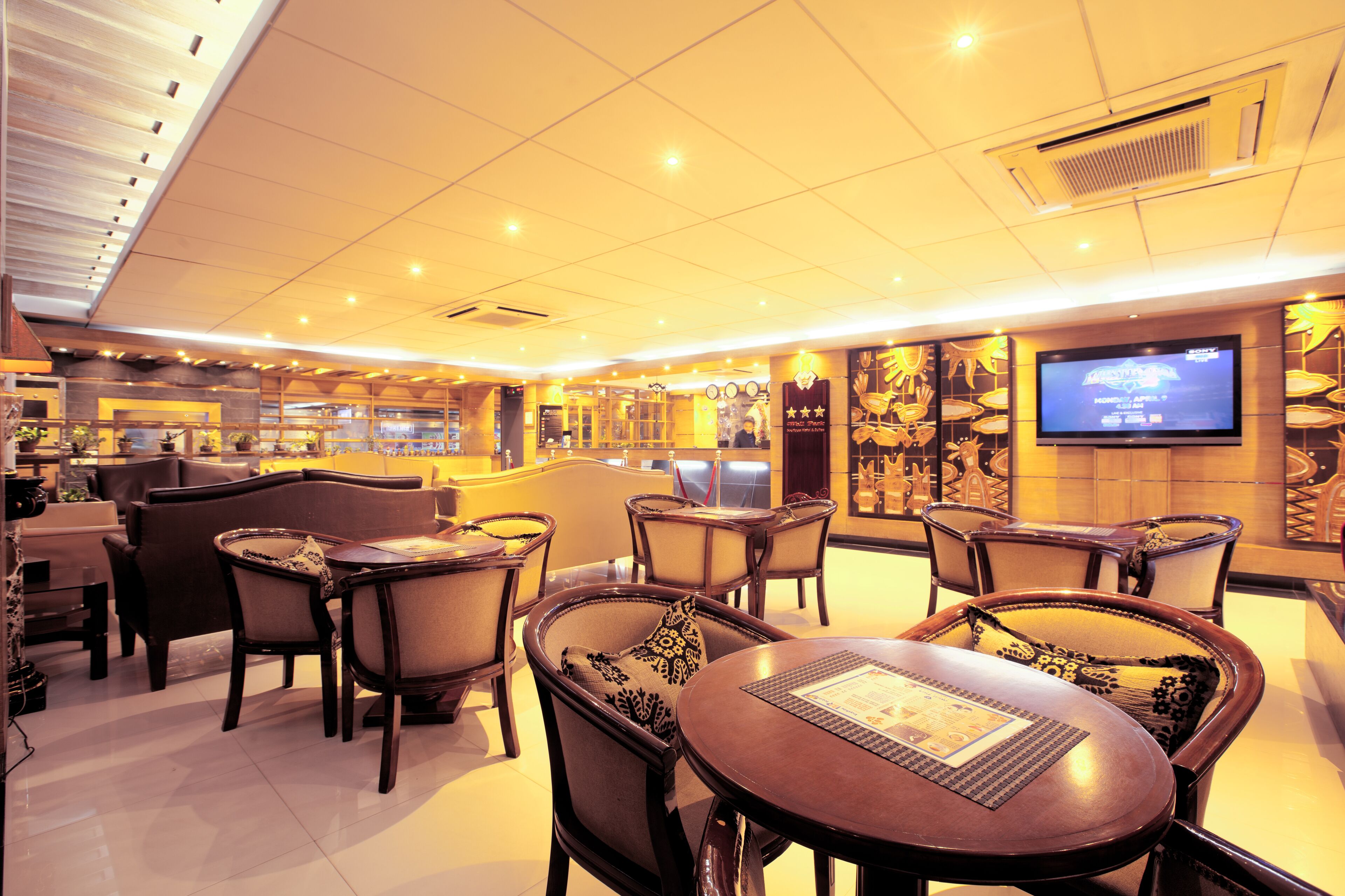 A restaurant interior with wooden tables and chairs, a television screen, and a ceiling with recessed lighting.
